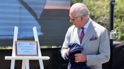 PA Media King Charles III unveils a plaque to officially launch the new UK Space Agency (UKSA) observatory. He turns to face the plaque while holding the cover